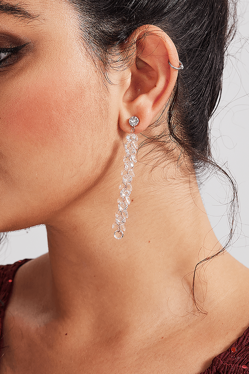 Close-up of Curveins Sparkle Gem Gold Bridgitte Earrings featuring cascading gold chains and crystal gems on a woman wearing a red dress.