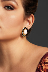 Close-up of elegant black-edged round pearl earrings featuring a bold black and gold-tone frame with a lustrous pearl centerpiece.