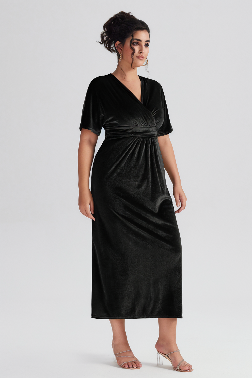 Side angle of the Curveins Plus Size Elegant Velvet V-Neck Shirred Maxi Dress in black, highlighting the elegant drape and midi length.